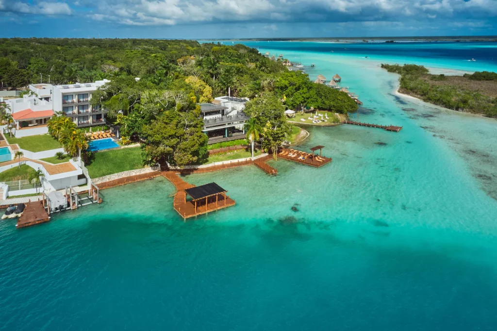 Aerial view of a tropical resort in Bacalar, Mexico, with a pier extending into turquoise waters, lush greenery, and surrounding coastline.